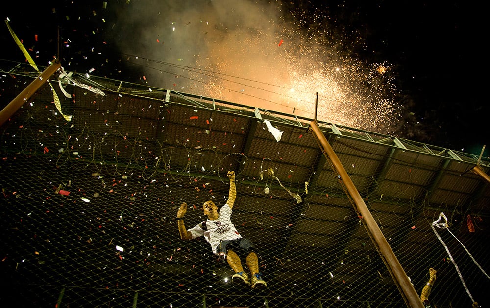 A fan of Argentina`s Lanus climbs a fence as fireworks explode outside the stadium before the Copa Sudamericana final soccer match against Brazil`s Ponte Preta in Buenos Aires, Argentina.
