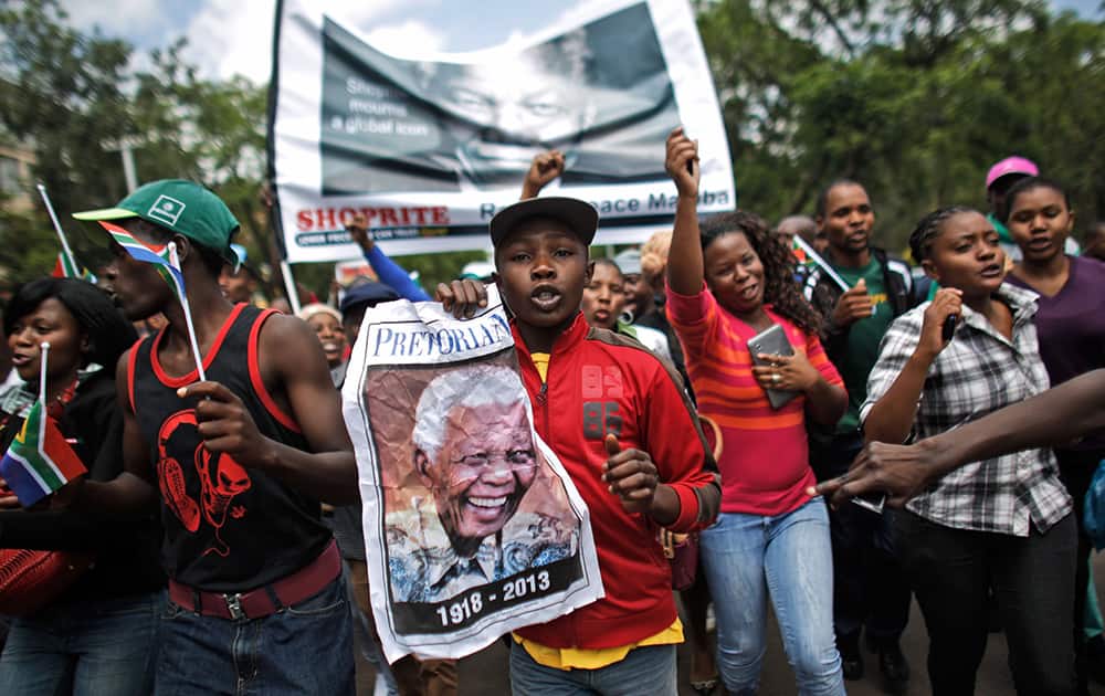 People carry pictures of former President Nelson Mandela as they sing and dance outside the Union Buildings grounds in Pretoria, South Africa.