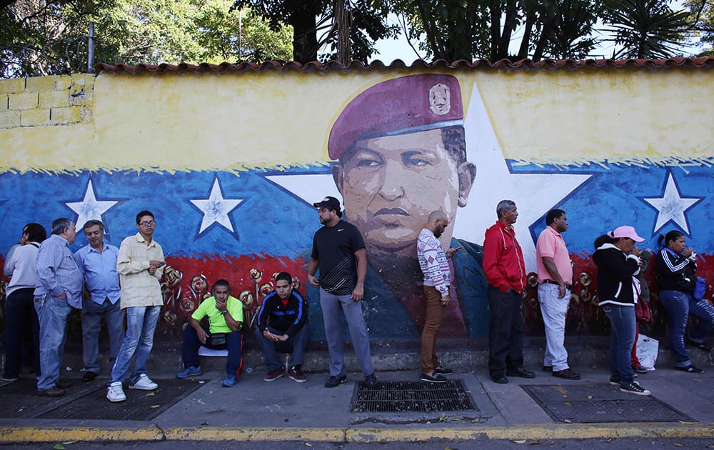 Residents wait in line to enter a polling station to vote in front of a wall painting depicting late president Hugo Chavez during municipal elections in Caracas, Venezuela.