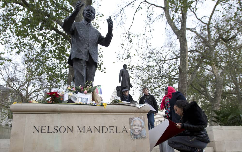 A woman writes on a card as flowers are laid in tribute at the foot of the Nelson Mandela statue in Parliament Square, London.
