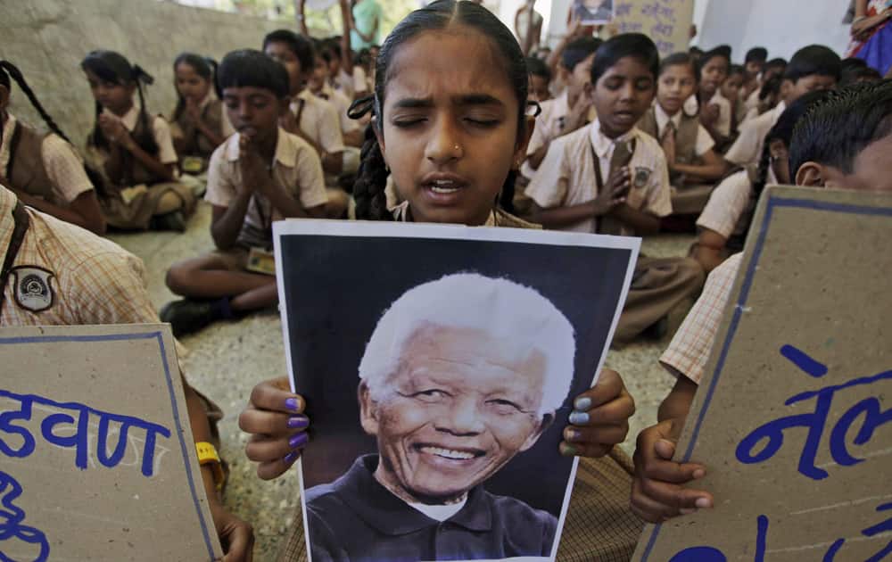 A young Indian school girl holds a portrait of former South African president Nelson Mandela as she prays along with others on hearing of his death, at a school in Ahmadabad.