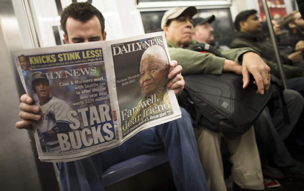 A subway rider reads a newspaper featuring news of the death of South African leader Nelson Mandela in New York.