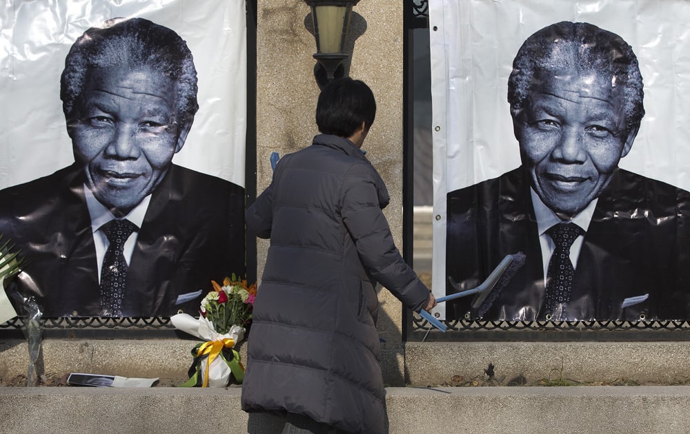 A woman cleans up outside the South African Embassy where portraits of former South African President Nelson Mandela and flowers offered by people are placed, in Beijing.
