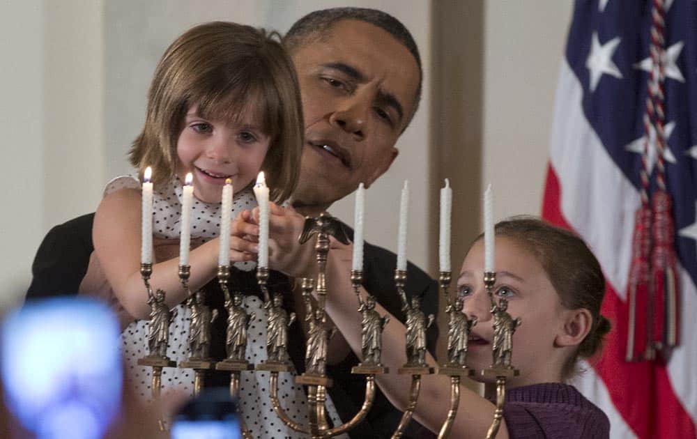 President Barack Obama holds up Kylie Schmitter as she and her sister Lainey Schmitter, lights the menorah during the first of two Hanukkah receptions in the Grand Foyer of the White House in Washington.