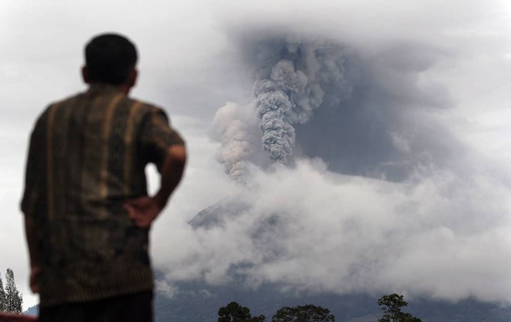 A man watches as Mount Sinabung erupts in Gundaling, North Sumatra, Indonesia. About 15,000 people have been evacuated from 17 villages on the slope of Mount Sinabung after authorities raised the alert status of the rumbling volcano to the highest level on Nov. 24.