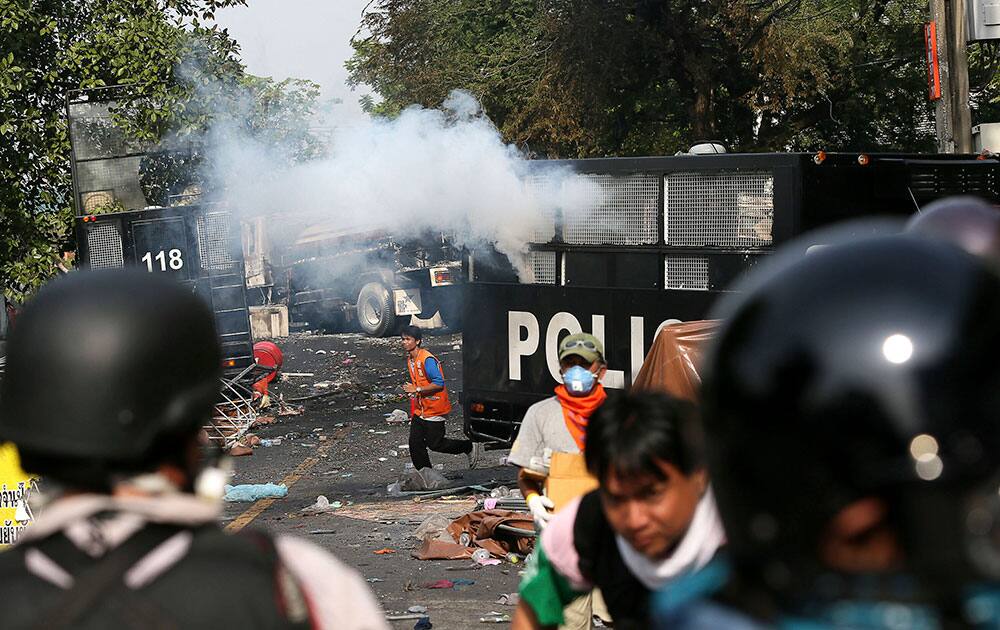 Anti-government protesters run for cover after police fires a tear gas shell to disperse them during a protest rally outside government offices which are barricaded by police forces, in Bangkok, Thailand.