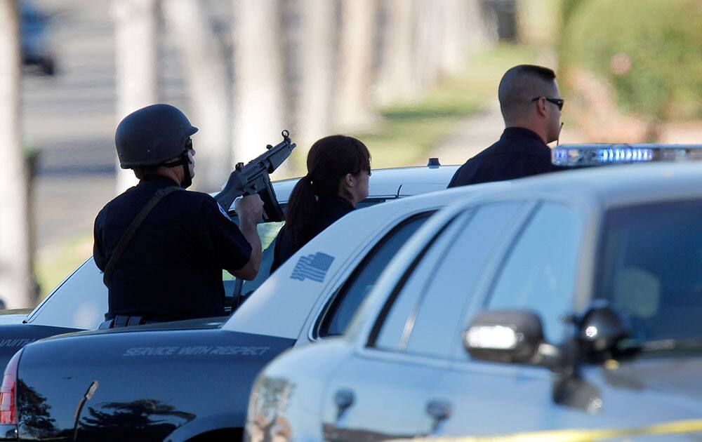 Inglewood police officers take up positions outside a residence, Wednesday, Nov. 27, 2013, in Inglewood, Calif., where a police officer was shot and another received minor injuries in a confrontation with a gunman who barricaded himself inside a home and could be holding a hostage, authorities said.
