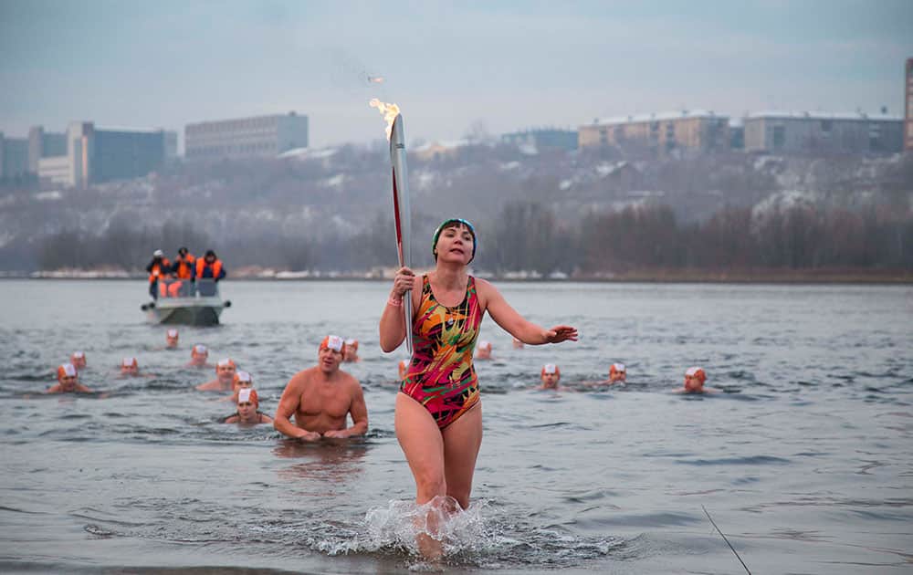 Torch bearer Natalia Usacheva, ice cold water swimmer, exits the Tatyshev Channel of the Yenisei River with an Olympic torch during the Olympic torch relay in Krasnoyarsk, Russia.