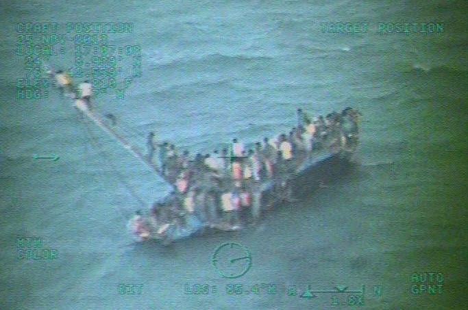 This image taken from video made available by the U.S. Coast Guard shows a group of Haitian migrants sitting on the hull of a capsized sailboat near Staniel Cay, Bahamas.
