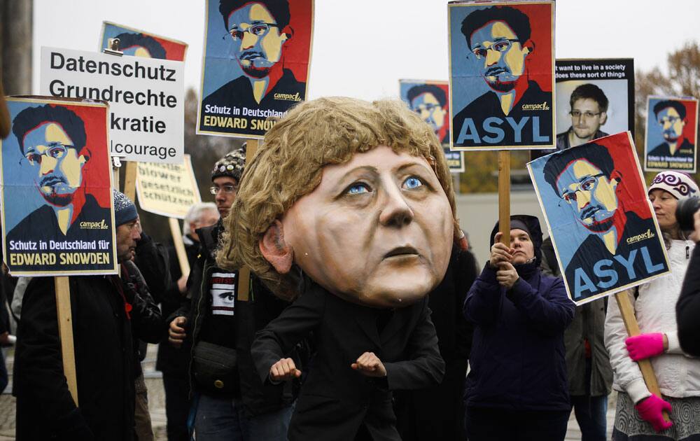 A demonstrator with a mask depicting German Chancellor Angela Merkel poses in front of other protesters holding posters of former National Security Agency NSA member Edward Snowden outside the German parliament building prior to a special meeting of the parliament on US German relationships, in Berlin.