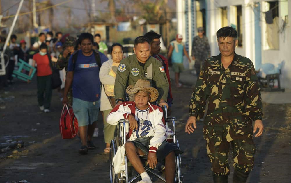 Filipino military personnel assist an elderly individual in a wheel chair as typhoon survivors queue up to get onto an evacuation flight to leave the typhoon-ravaged city of Tacloban, in the Philippines.