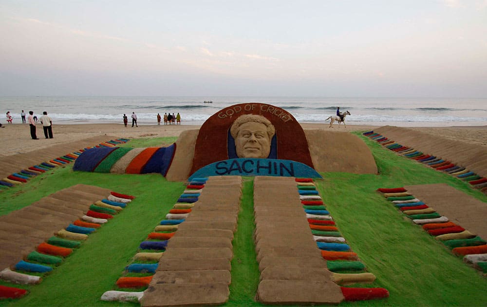 An Indian man rides a horse past a sand sculpture of Indian cricket player Sachin Tendulkar created by Sudarshan Pattnaik on a beach in Puri.