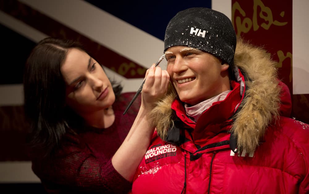 A Madame Tussauds artist poses for photographers with a waxwork of Britain`s Prince Harry dressed for a trek to the South Pole during a photocall at the attraction`s premises in London.