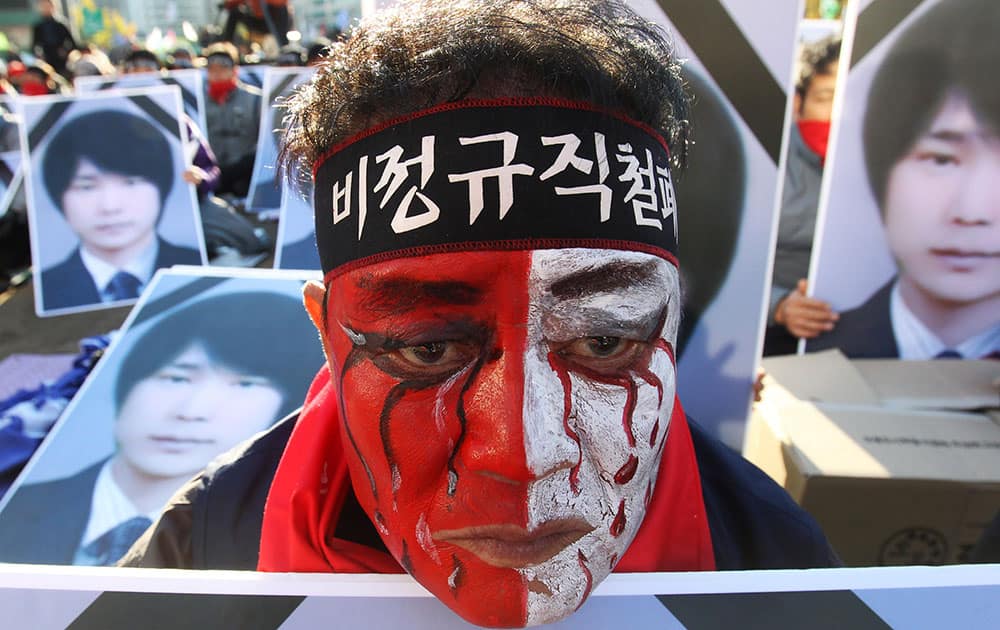 A worker with his face painted, stands in front of portraits of Choi Jong-beom as he participates in a rally against government`s labor policy in front of the Seoul City Hall in Seoul, South Korea.