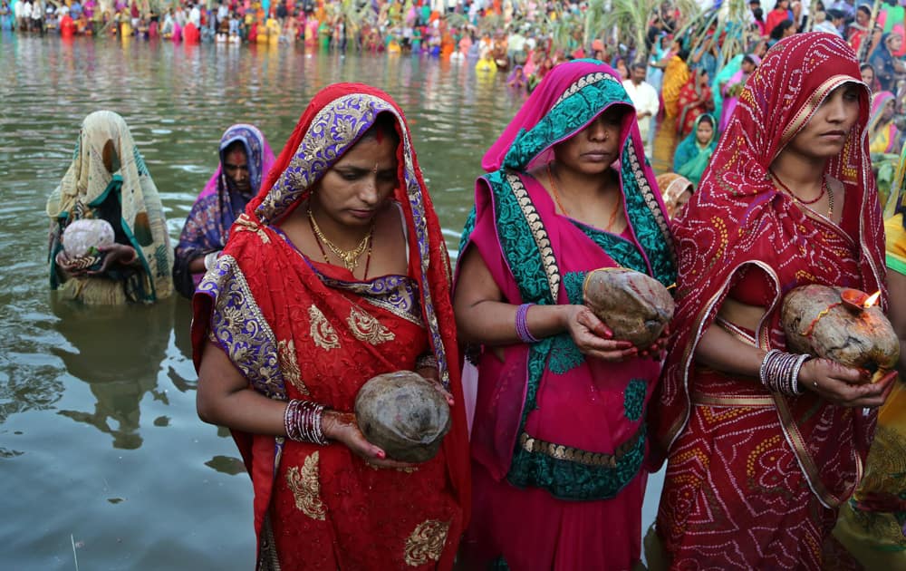 Hindu devotees hold coconuts as they stand in water to perform rituals to the setting sun during Chhath Puja festival in Bangalore.