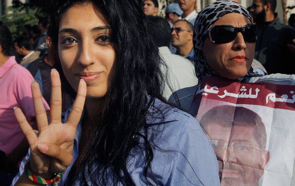 A supporter of Egypt`s ousted President Mohammed Morsi raises her hand with four raised fingers, which has become a symbol of the Rabaah al-Adawiya mosque, where Morsi supporters had held a sit-in for weeks that was violently dispersed in August, as another holds his poster with Arabic that reads,