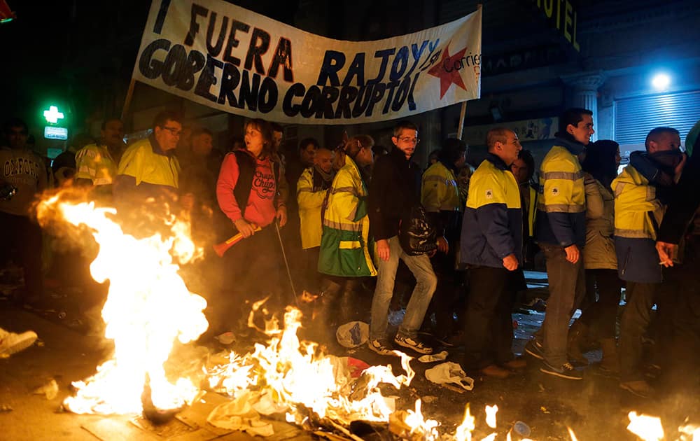 Protestors burn trash as they carry a banner reading