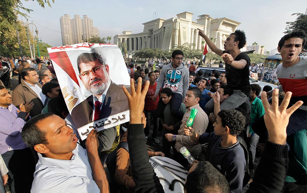 Supporters of Egypt`s ousted President Mohammed Morsi raise their hands with four raised fingers, which has become a symbol of the Rabaah al-Adawiya mosque, where Morsi supporters had held a sit-in for weeks that was violently dispersed in August, as one holds his poster during a protest against Morsi`s trial in front of the supreme constitutional court in Cairo, Egypt.
