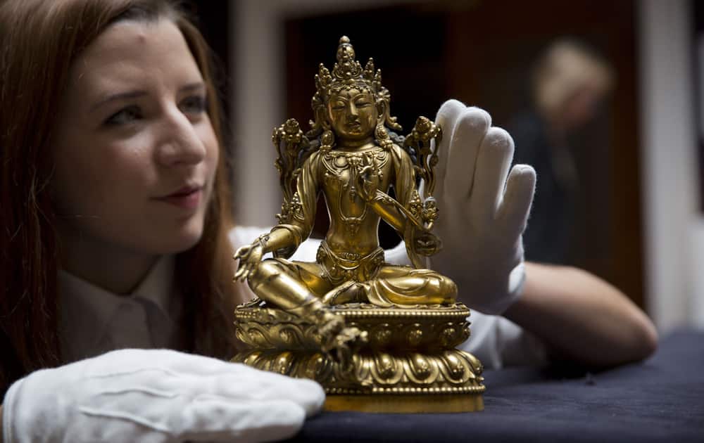 A Sotheby`s employee poses for photographs with a gilt-bronze figure of Shyama Tara, Ming Dynasty, from the early 15th century at the auction house`s premises in London.
