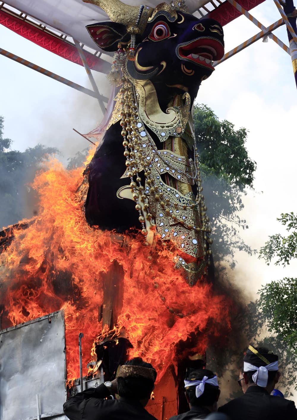 Balinese men watch a giant sarcophagus in the form of a bull which contains the body of Tjokorda Gde Raka Sukawat is in flame during a cremation ceremony of a descendant of the Ubud Royal family in Bali, Indonesia.