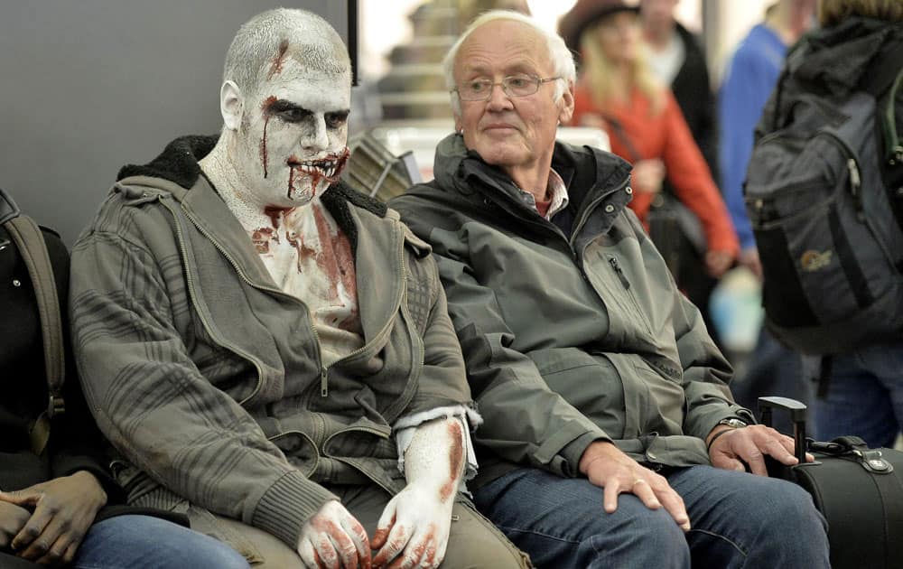 A man waiting at the train station looks at another wearing Halloween themed make-up in the city center of Essen, western Germany.