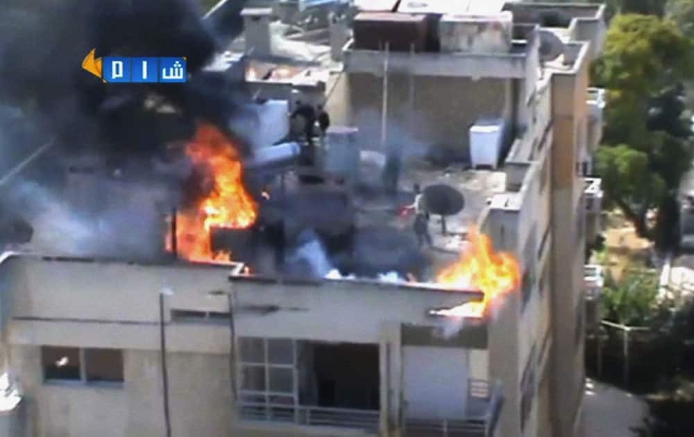 This image taken from video obtained from the Shaam News Network, which has been authenticated based on its contents and other AP reporting, people try to extinguish a fire on the roof of a building, allegedly caused by shelling in Homs, Syria.