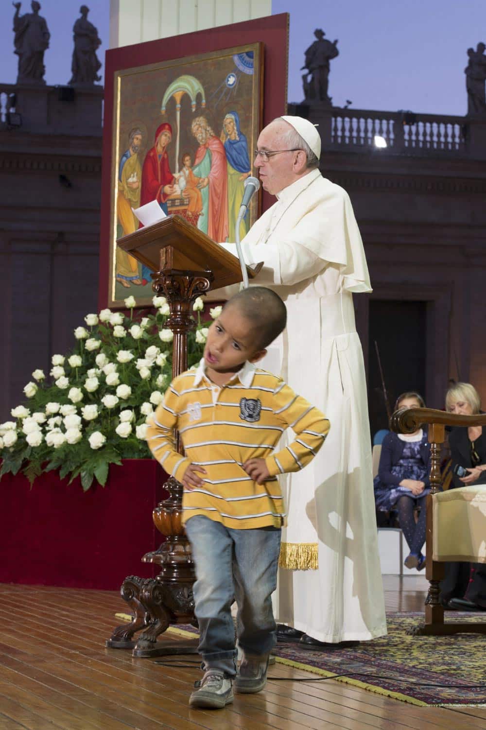 This photo provided by the Vatican newspaper L`Osservatore Romano, Pope Francis reads his message as a young boy plays in front of him on the stage during an audience with families in St. Peter`s Square, gathered for the Pontifical Council for the Family`s plenary assembly, at the Vatican.