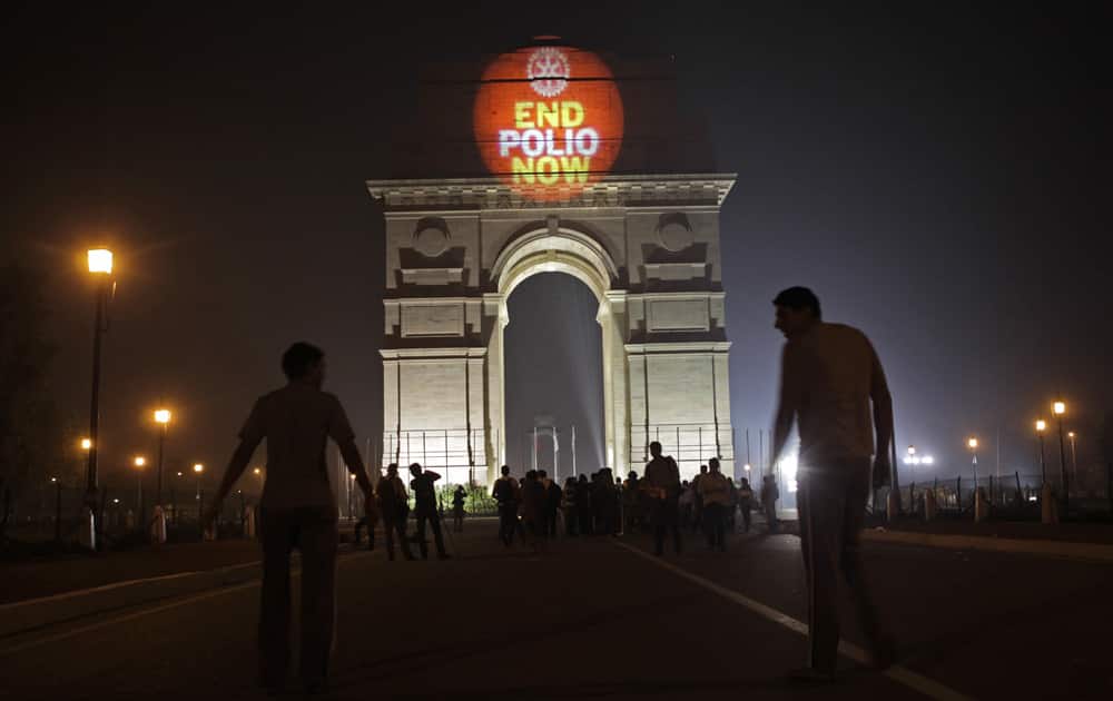 People walk past as a laser beam is projected on the India Gate monument as part of an awareness campaign on World Polio Day in New Delhi.