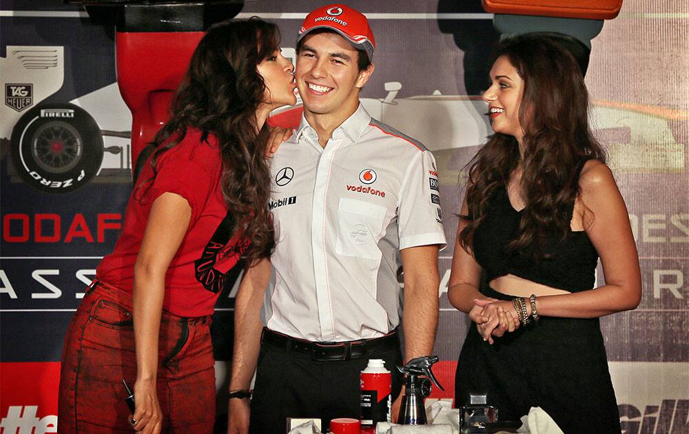 Bollywood actress Neha Dhupia kisses the cheek of McLaren Formula One driver Sergio Perez of Mexico as Aditi Rao Hydari stands beside him during a promotional event, in New Delhi.