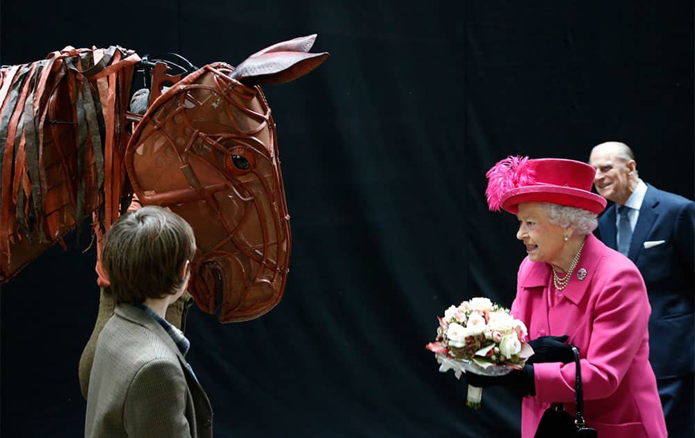 Britain`s Queen Elizabeth II, accompanied by The Duke of Edinburgh, right, receives flowers from a child actor as she inspects the horse prop from the theatre production `War Horse` during a visit at the National Theatre in London.