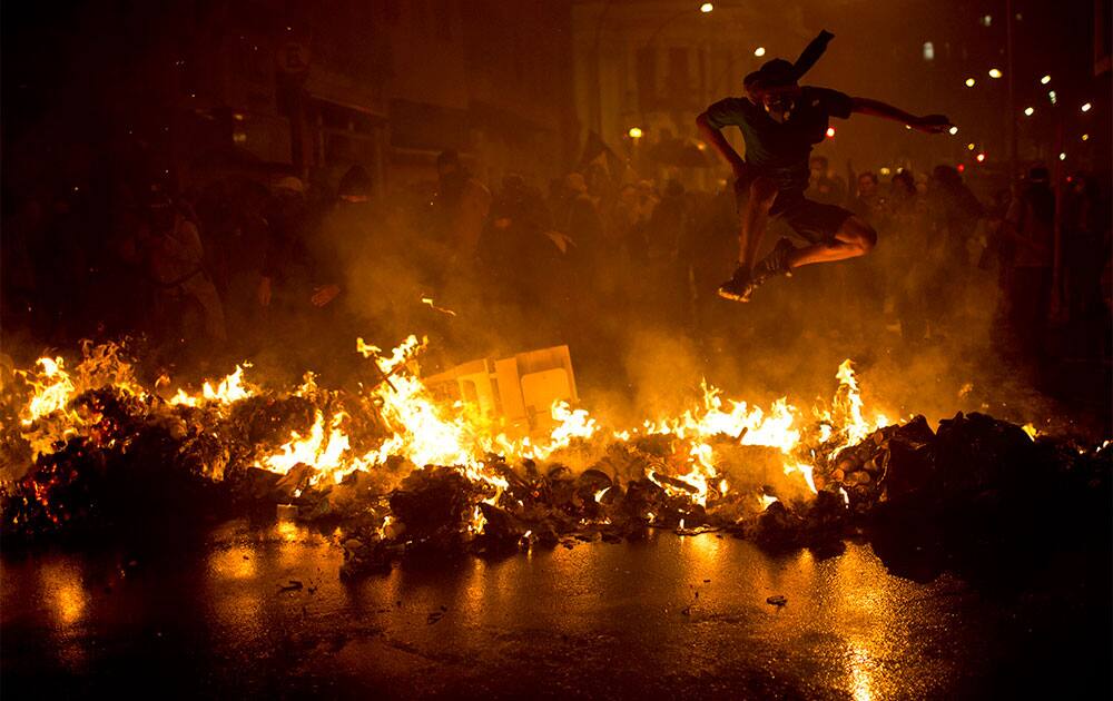 A Black Bloc anarchist jumps over a burning barricade at the Cinelandia square during a march in support of teachers on strike in Rio de Janeiro, Brazil.