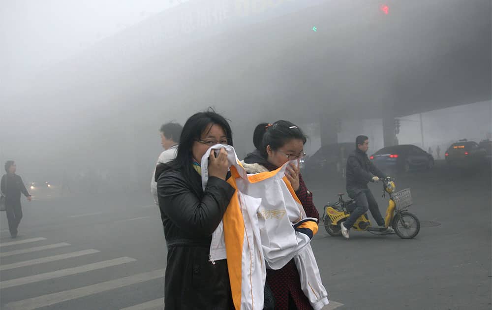 Two women cover up their mouths and noses with a jacket as they cross a street covered by dense smog in Harbin, northern China.