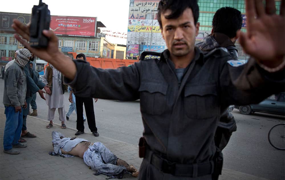 An Afghan police man pushes people away after a bomb exploded under a car, leaving the driver dead, in the center of Kabul.