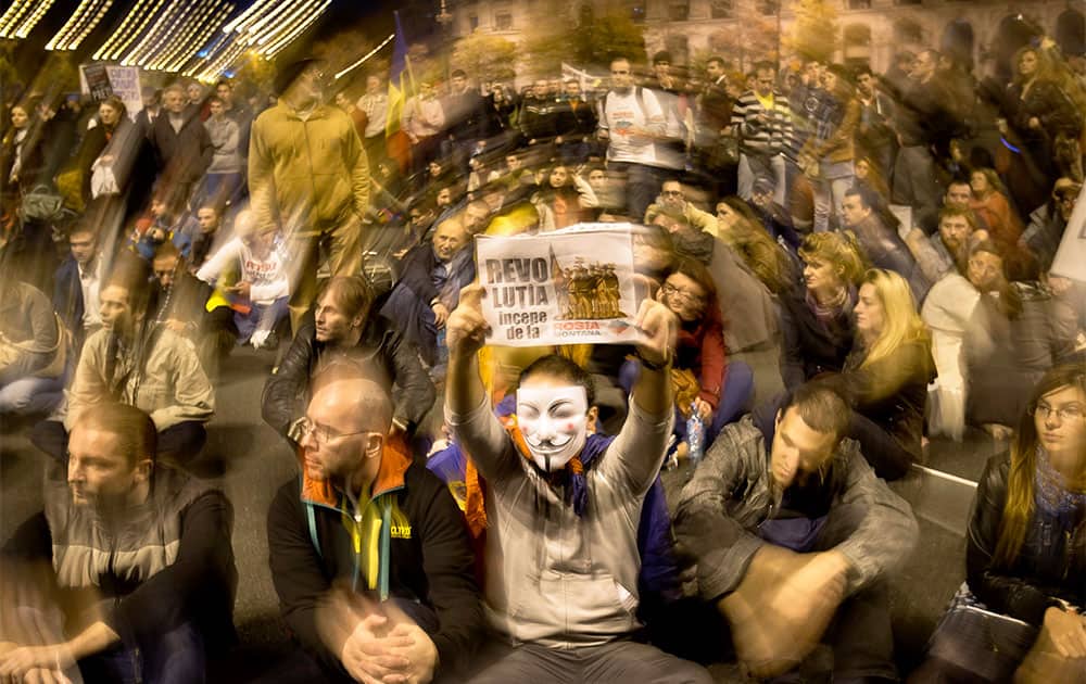Protesters, one wearing a Guy Fawkes mask and holding a poster that reads