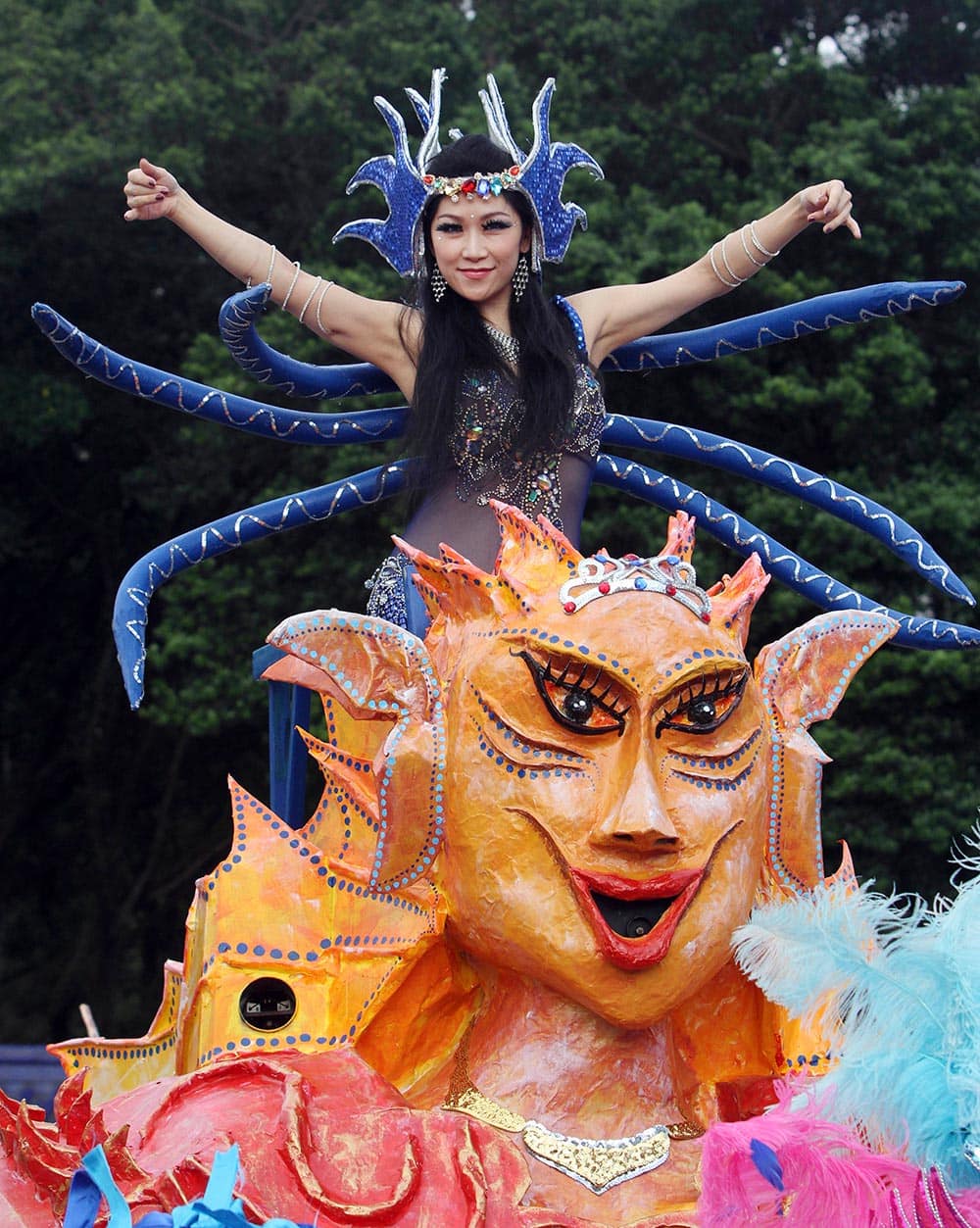 A costumed woman performs atop a float in a street during the