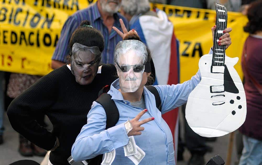 A protester wears a homemade mask depicting Uruguay`s President Jose Mujica holding a cardboard interpretation of the guitar given to the leader by Aerosmith frontman Steven Tyler.