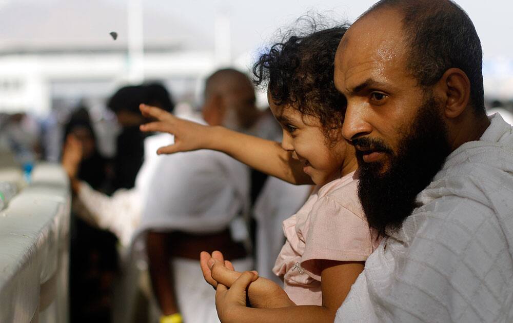 A Muslim pilgrim carries his son as they cast stones at a pillar, symbolizing the stoning of Satan, in a ritual called