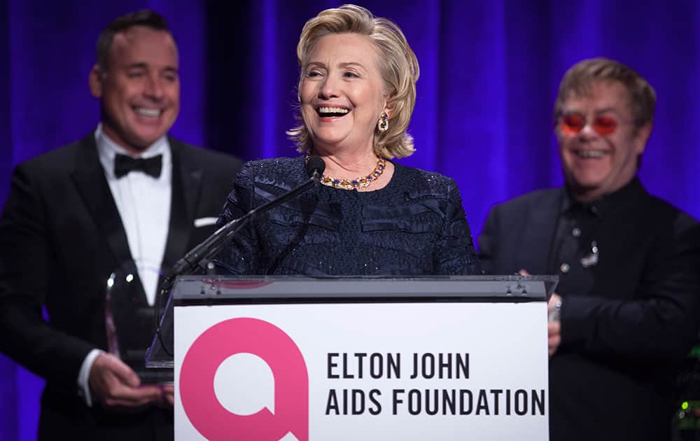 Former Secretary of State Hillary Clinton speaks as Elton John and his partner David Furnish look on, after receiving her Founders award during the Elton John AIDS Foundation`s 12th Annual