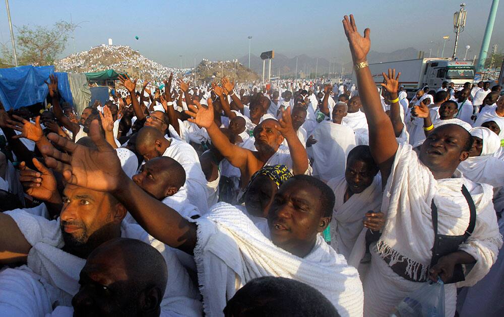 Muslim pilgrims raise their hands to receive umbrellas in front of a rocky hill called the Mountain of Mercy, on the Plain of Arafat near the holy city of Mecca, Saudi Arabia.