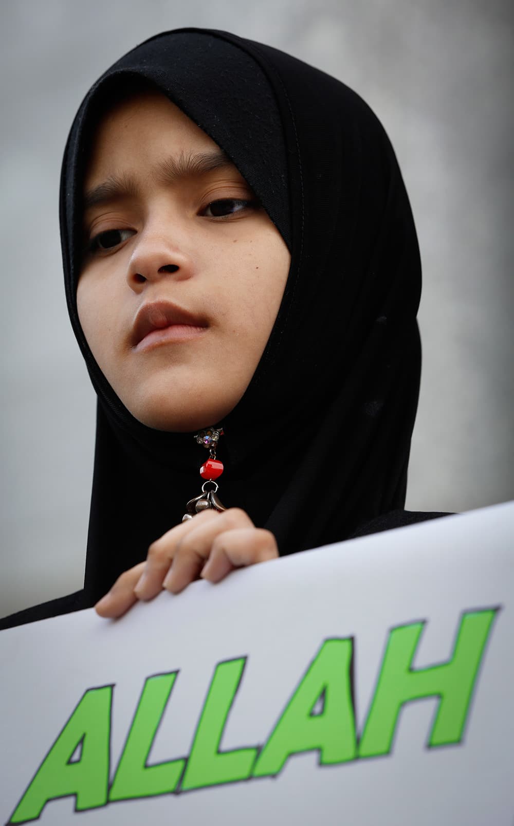 A Muslim woman holds a banner reading