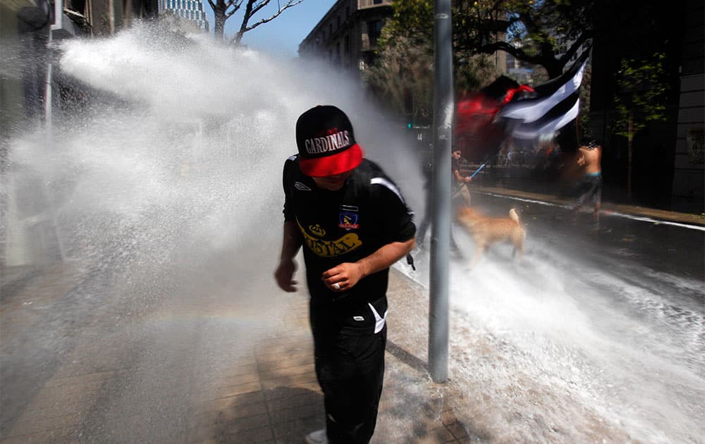 A protester runs away from a police water cannon after clashes broke out at a march against the commemoration of the discovery of America in Santiago, Chile.