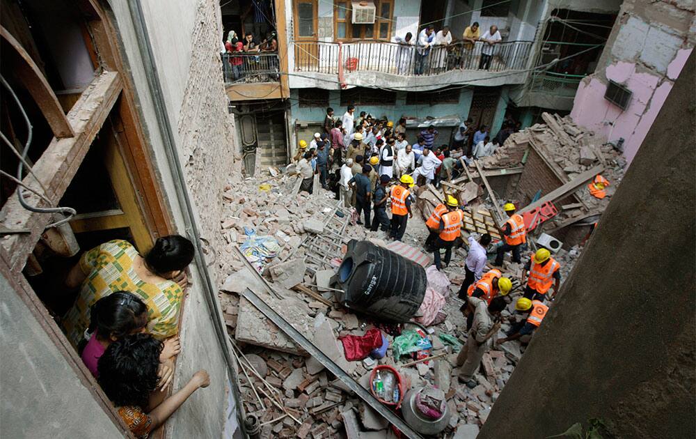 Women watch from the window of their house as rescue workers clean up the debris of a collapsed building in New Delhi. The three-story home that collapsed in India’s capital was located in a crowded residential area of northern New Delhi, where narrow roads made rescue and cleanup efforts difficult. Two people are reported dead.