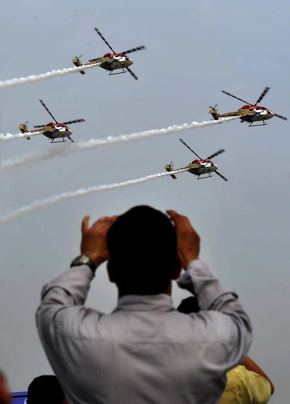 An Indian man snaps photos as Indian Air Force (IAF) Sarang helicopters perform an aerial display during Air Force Day at Hindon, on the outskirts of New Delhi.