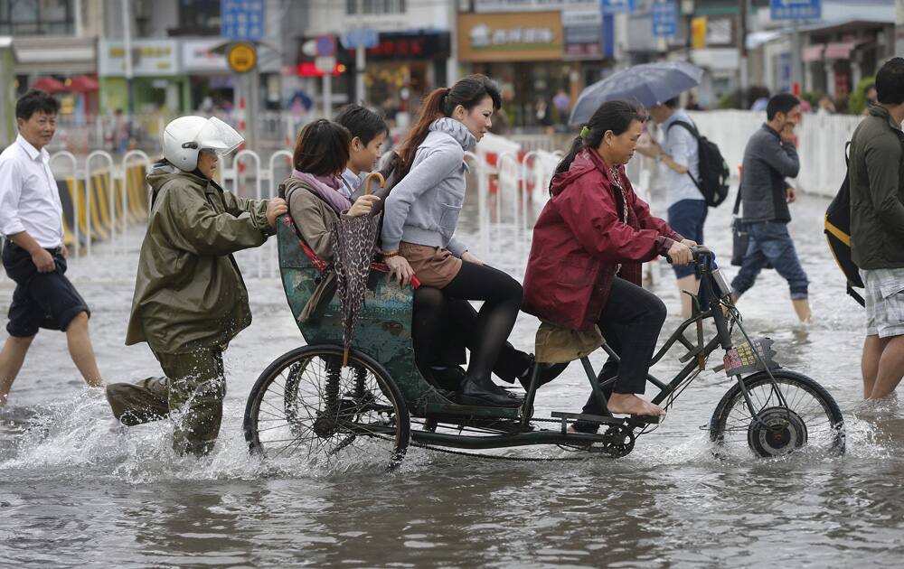 Commuters ride on a tricycle cross a flooded road outside a subway station in Shanghai, China.