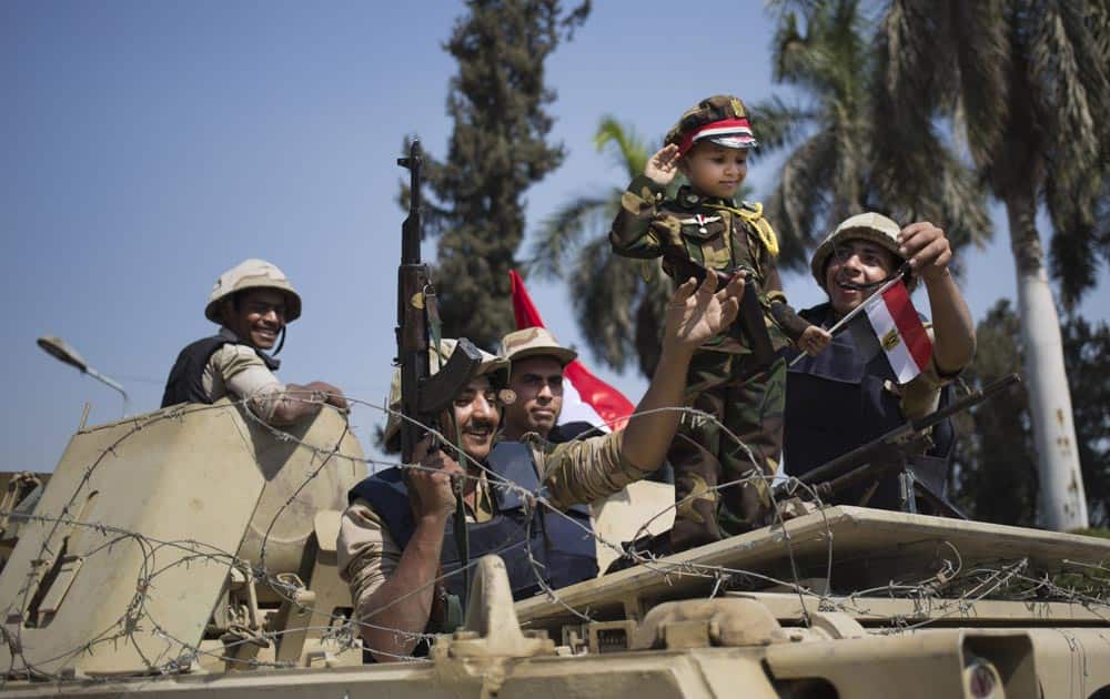 An Egyptian boy in an army costume salutes while posing next to army soldiers, from atop an armored vehicle guarding an entrance to Tahrir Square, in Cairo.