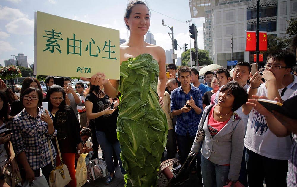 A member of People for the Ethical Treatment of Animals (PETA) poses in a gown made of lettuce leaves and holds a sign that reads,