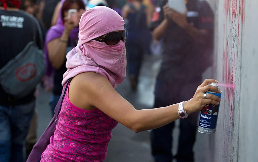 A masked protester spray paints a wall during a march commemorating the anniversary of the Tlatelolco massacre in Mexico City.