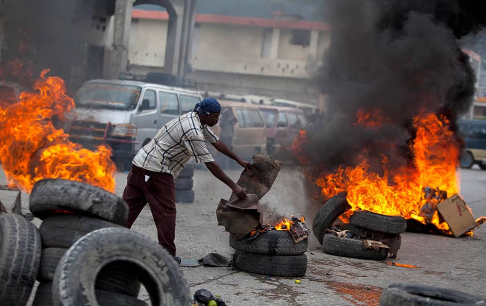 A demonstrator adds cardboard to burning tires blocking the capital`s main street during a protest against the government of President Michel Martelly in Port-au-Prince, Haiti.
