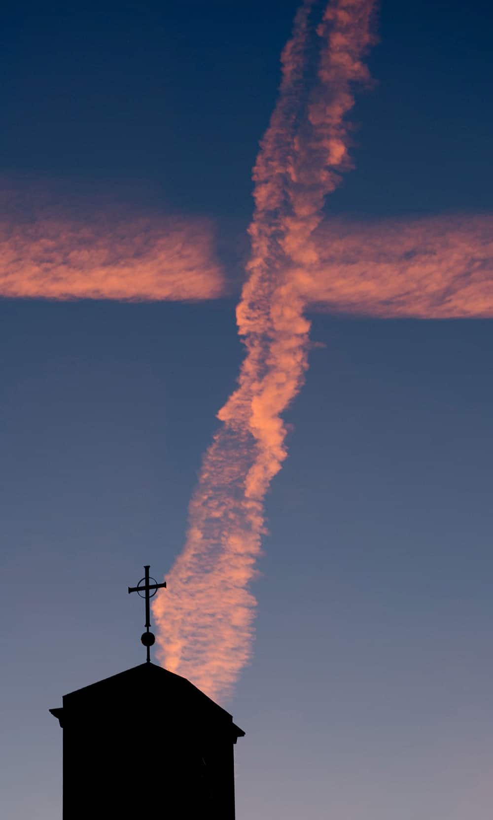 Condensation trails of planes cross above a church during sunrise in Hannover, northern Germany.