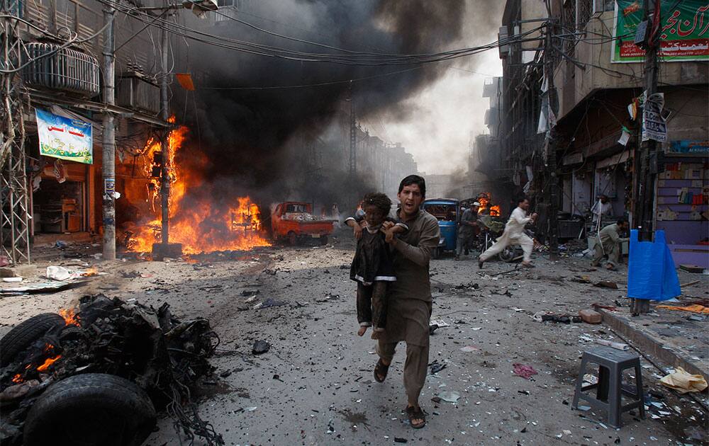 A man carrying a child rushes away from the site of a blast shortly after a car exploded in Peshawar, Pakistan. A car bomb exploded on a crowded street in northwestern Pakistan, killing scores of people in the third blast to hit the troubled city of Peshawar in a week, officials said.